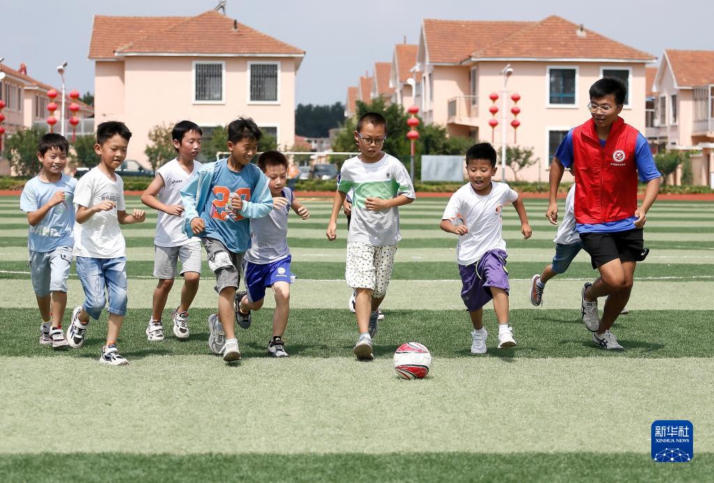 7月18日，在山东省青岛市即墨区龙山街道前东葛村，山东理工大学大学生志愿者姜昊（右一）与孩子们一起踢足球。