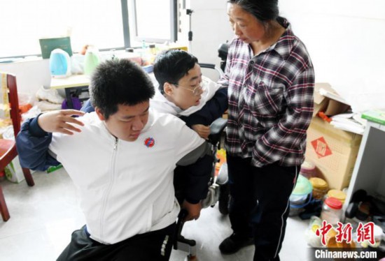 江西省南康中学北校区的高三学生朱金祥(左)来到学校给钟华强母子安排的公寓，准备背他去课堂上课。　 卓忠伟 　摄